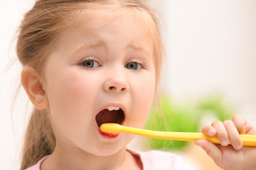 Cute little girl brushing teeth on blurred background
