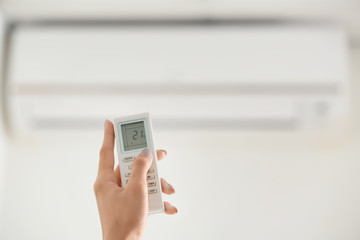 Young woman pointing remote control at air conditioner indoors