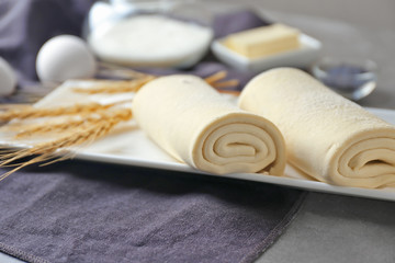 Fototapeta na wymiar Plate with rolled flaky dough on table
