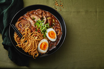 Japanese ramen with pork belly, mushrooms and marinated eggs on green linen tablecloth. Horizontal composition with copy space