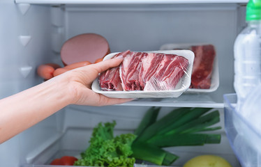 Woman putting raw meat in refrigerator, closeup