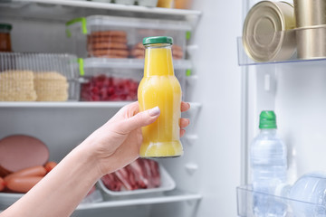 Woman holding bottle of juice near open refrigerator, closeup