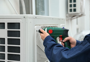 Male technician fixing air conditioner outdoors