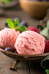 Raspberry ice cream scoops in copper bowl with forest berries and mint decoration. Summer food concept. Macro shoot.