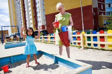 Fototapeta na wymiar Tranquil granny and her little granddaughter shouting on the playground.