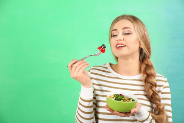 Young beautiful woman eating fresh salad on color background