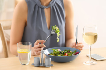 Young woman eating fresh salad at table