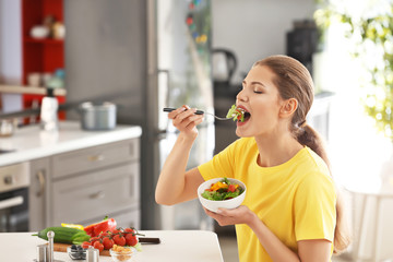 Young beautiful woman eating fresh salad in kitchen