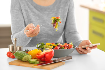 Young beautiful woman with phone eating fresh salad at table