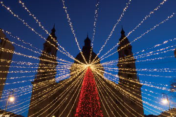 Fototapeta premium Lighting garland over Christmas tree against st. Stephen's Basilica outline in Budapest