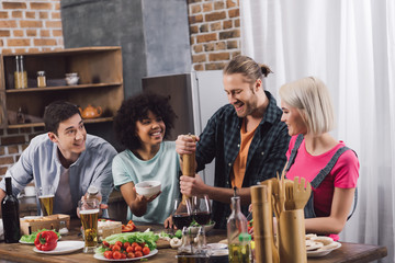 multiethnic friends looking how man adding spice to food with pepper grinder