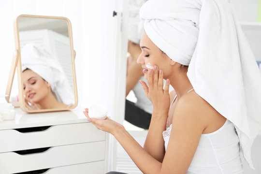 Attractive young woman applying face cream in bathroom