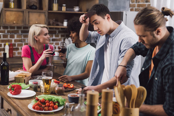 multiethnic girls drinking wine while men cooking in kitchen