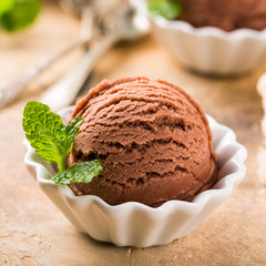 Chocolate ice cream scoop in white bowl with mint leaves on sand color stone background. Summer food concept. Macro shoot.