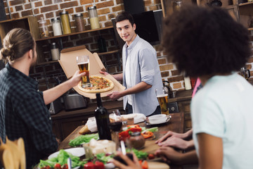 happy man showing homemade pizza to multiethnic friends