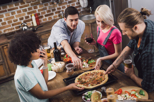 Multicultural Friends Eating Homemade Pizza In Kitchen