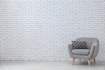 Comfortable armchair near white brick wall