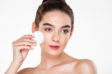 Close up beauty portrait of brunette attractive woman cleaning her face with cotton pad isolated over white background