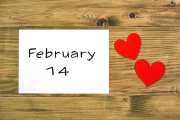 February 14 text on the white paper and heart shapes on wooden table.