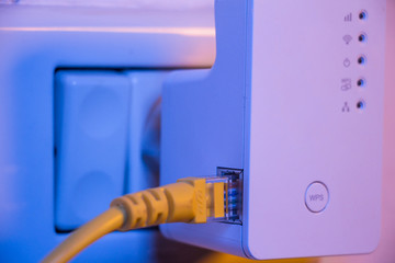 WiFi extender in electrical socket on the wall with ethernet cable plugged in