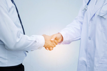 friendly female doctor with stethoscope around her neck shaking hands with medium aged male patient for reassuring in hospital, assistance, medical, people, age, health care and support concept