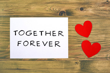 White paper with text together forever and heart shapes on wooden table.