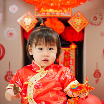 Chinese baby girl with traditional dressing up celebrate Chinese new year.some "FU" mean "lucky"greeting card on the wall