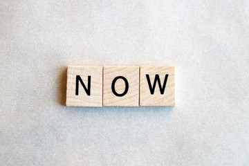 Wood squares spell the word now, flat lay on white background.