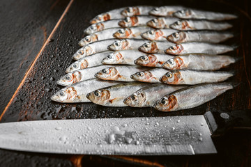 fresh raw fish anchovy and sprat on a wooden surface with a cutting knife