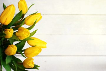 Spring decorative composition. Bouquet of yellow tulips tied by green ribbon. Close up portrait on white wooden background