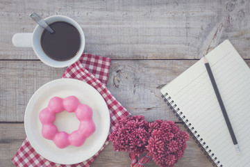 Top view,Opened notepad and cup of coffee with donut on wood background.