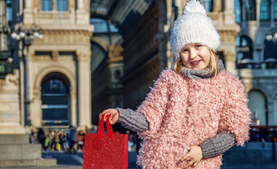 happy elegant child showing red shopping bag in Milan, Italy