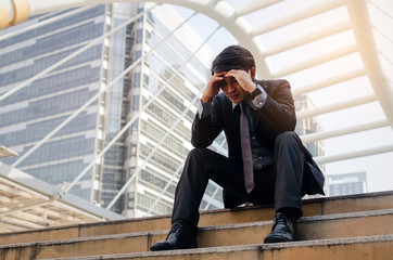 disappointed, sadness or stressed medium aged unemployed business man with briefcase sitting on walkway in the city after fired from job, business problem, unemployment, financial, investment concept