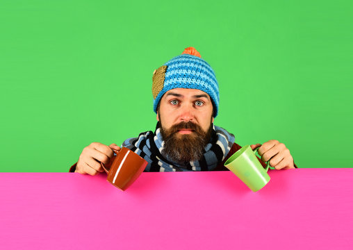 Man in warm hat holds brown and green cups