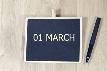 sentence MAR 1 written with chalkboard on a wooden table with pen.