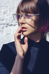 beautiful stylish woman with pink hair and glasses touching lips with hand