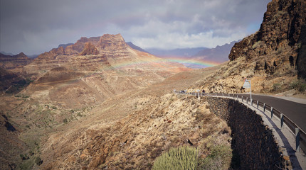 Rainbow over road into mountain landscape of Gran Canaria island, Spain / Valley of "Fataga" seen from the viewpoint "Degollada de la yegua"