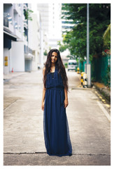 Naklejka premium Portrait of young Indian Asian woman standing in the middle of the street wearing a long blue dress looking at the camera. 