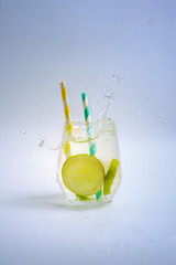 Cup with splashing lime water and paper straws, selective focus.