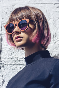 portrait of stylish girl with pink hair and sunglasses looking away