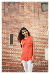 Portrait of attractive, young Indian woman standing in front of a brick wall in a city. She's laughing and is stylish. 