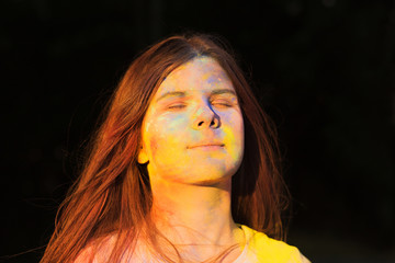 Pretty young woman covered with blue and yellow dry Holi powder posing in the park