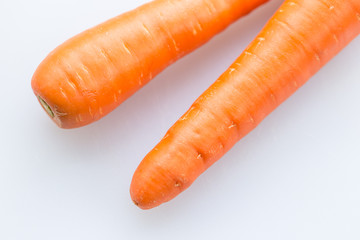 Pair long fresh raw carrot on a plastic cutting board is white color.