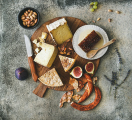 Flat-lay of cheese platter with cheese assortment, figs, honey, fresh bread and nuts over grey concrete background, top view. Party or gathering eating concept