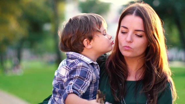 son kisses mother on the cheek in the park at sunset Mother and her little son outdoors, Happy family mom and kid kissing and hugging. Slow motion, high speed camera shot. Full HD 1080p