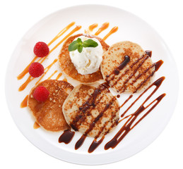 Serving pancakes with ice cream on the plate. Decorated with chocolate syrup, caramel syrup, fresh berries and mint. Isolated on white background. Top view.