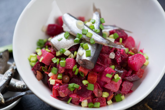 Close-up of russian vinegret or vinaigrette topped with sprats and green onion, selective focus
