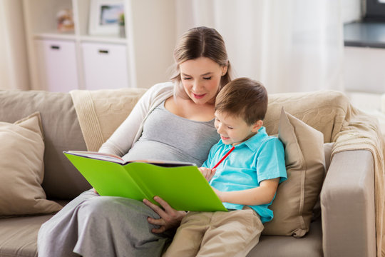 pregnant mother and little son with book at home