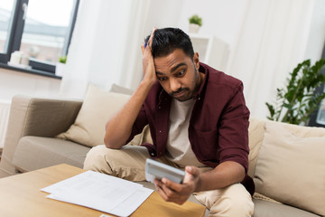 confused man with papers and calculator at home