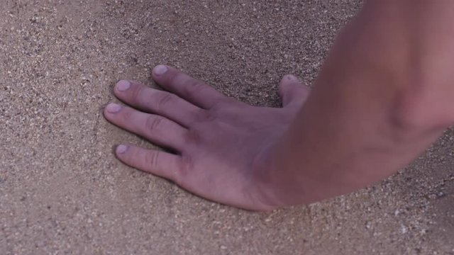 Close up of man's hand touching sand at the shore of the sea - concept of native place. man holds his hand over the sand on the beach - concept of vacations and tourism. Sand on the hand at green sand